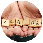 Zwei Hände halten hölzerne Scrabble-Steine mit dem Wort „SENIOR“. Der Hintergrund ist unscharf, wodurch die Steine hervorgehoben werden. Das Bild hat einen kreisförmigen Rahmen.