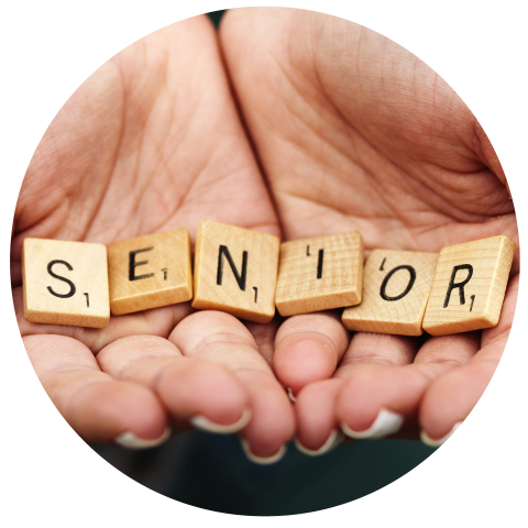 Zwei Hände halten hölzerne Scrabble-Steine mit dem Wort „SENIOR“. Der Hintergrund ist unscharf, wodurch die Steine hervorgehoben werden. Das Bild hat einen kreisförmigen Rahmen.