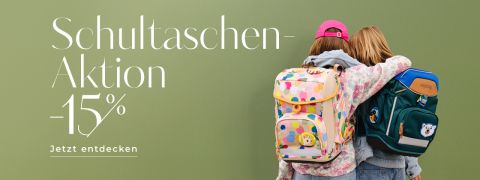 Zwei Kinder mit Rucksäcken stehen nebeneinander vor grünem Hintergrund. Ein Rucksack ist bunt mit Kreisen, der andere dunkelgrün mit Tieraufnähern. Links steht: „Schultaschen-Aktion -15%. Jetzt entdecken.“.