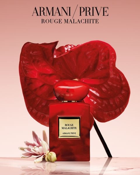 Ein roter Parfümflakon von Armani/Privé „Rouge Malachite“ mit tropischen Blumen vor einem rosa Hintergrund mit Farbverlauf.