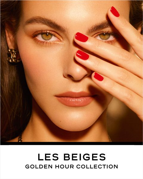 Eine Frau mit strahlender Haut hält ihre Hand mit rot lackierten Nägeln teilweise vor ihr Gesicht, zeigt goldbraune Augen und trägt goldene Ohrringe. Der Text darunter lautet: „Les Beiges Golden Hour Collection“.