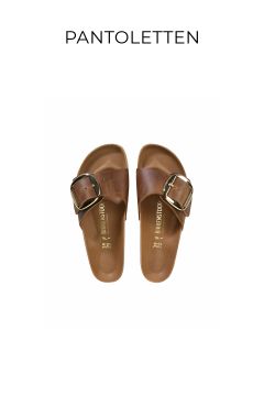 Ein Paar braune Slipper mit großen goldenen Schnallen, nebeneinander auf weißem Hintergrund. Über den Sandalen steht das Wort „PANTOLETTEN“.