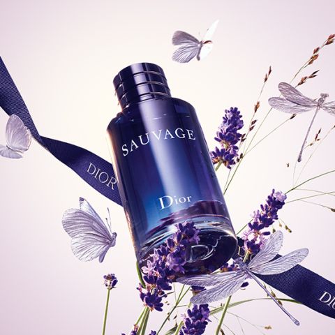 Eine Flasche Dior Sauvage ist von Lavendelzweigen, Schmetterlingen und einem dunklen Band mit der Aufschrift „Dior“ umgeben. Die Flasche ist tiefblau und trägt den weißen Aufdruck „SAUVAGE“.