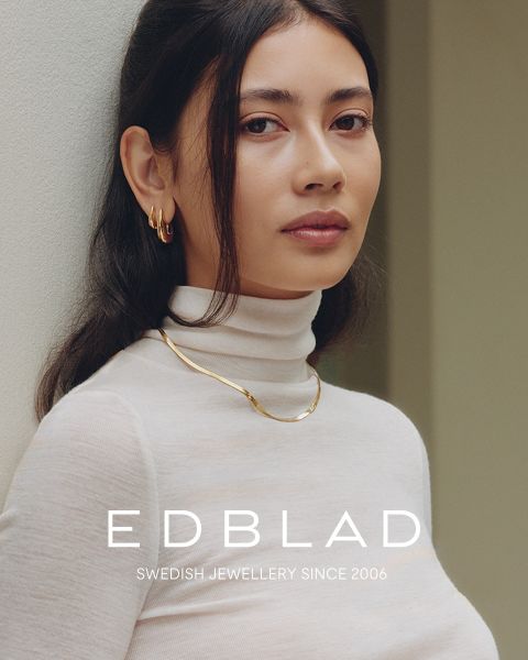 Eine Frau in einem weißen Rollkragenpullover trägt Goldschmuck. Der Text lautet: „EDBLAD SWEDISH JEWELLERY SINCE 2006.“.
