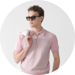 Ein Mann mit dunkler Sonnenbrille und einem hellrosa gemusterten Poloshirt hat sich einen hellen Pullover über die Schulter gelegt und steht vor einem schlichten weißen Hintergrund.
