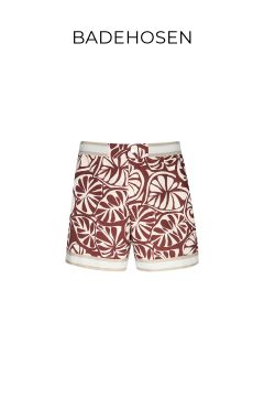 Eine Badehose mit einem auffälligen, kastanienbraun-weißen, abstrakten Blattmuster, einem cremefarbenen Bund und Besatz. Über der Shorts steht der Schriftzug „BADEHOSEN“.
