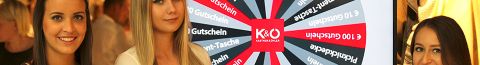 Drei Frauen in weißen G-STAR-Shirts halten Tablets vor einem „Glücksrad“-Display in einem Geschäft. Auf dem Rad sind verschiedene Preise wie Gutscheine und Rabattaktionen zu gewinnen.