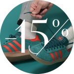 Eine Person bindet die Schnürsenkel blaugrüner und roter Adidas-Sneaker. Sie trägt beige Hosen und weiße Socken. Über dem Bild liegt ein großer Text „-15 %“ und weist auf einen Rabatt oder eine Aktion hin.