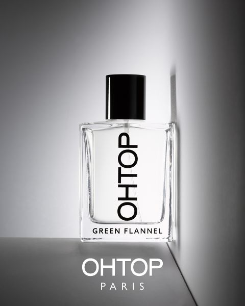 Der Parfümflakon mit der Aufschrift „OHTOP GREEN FLANNEL“ steht auf einer grauen Fläche vor hellgrauem Hintergrund. Die Flasche ist teilweise beschattet, darunter steht der Schriftzug „OHTOP PARIS“. Minimalistisches Design mit schwarzem Verschluss.