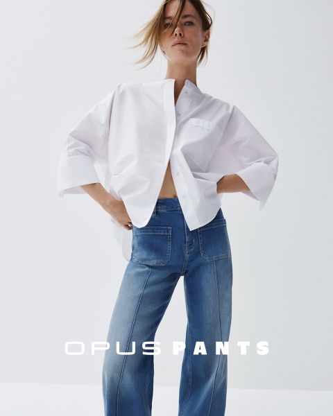 Person in lockerem weißen Hemd und Bluejeans, die Hände in die Hüften gestemmt. Unten steht der Text „Opus Pants“. Das Haar ist leicht vom Wind zerzaust, weißer Hintergrund.