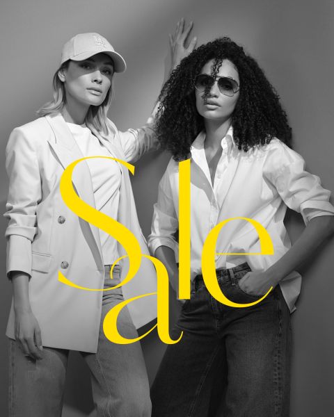 Zwei stylische Frauen in lässigen Outfits posieren selbstbewusst; die eine trägt Cap und Blazer, die andere Sonnenbrille und weißes Shirt. Darüber steht in großem gelben Text „Sale“. Bis auf den Text ist das Bild schwarz-weiß.