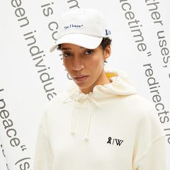 Eine Person mit einem weißen Kapuzenpullover mit der Aufschrift „8IW“ und einer weißen Kappe mit der Aufschrift „Ja, ich weiß*“ steht vor einem Hintergrund mit großem, teilweise sichtbarem Text.