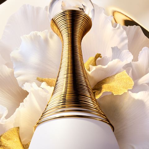 Eine Nahaufnahme eines luxuriösen Parfümflakons mit einem goldenen, spiralförmig umwickelten Hals vor einem Hintergrund aus weichen, weißen Blütenblättern, akzentuiert mit einem Hauch von Gold.