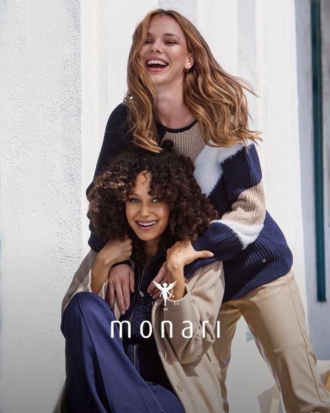 Zwei Frauen lächeln und lachen im Freien. Eine steht hinter der anderen und hat die Hände auf den Schultern. Sie tragen stilvolle, lässige Outfits. Unten steht der Schriftzug „Monari“ zusammen mit dem Markenlogo.