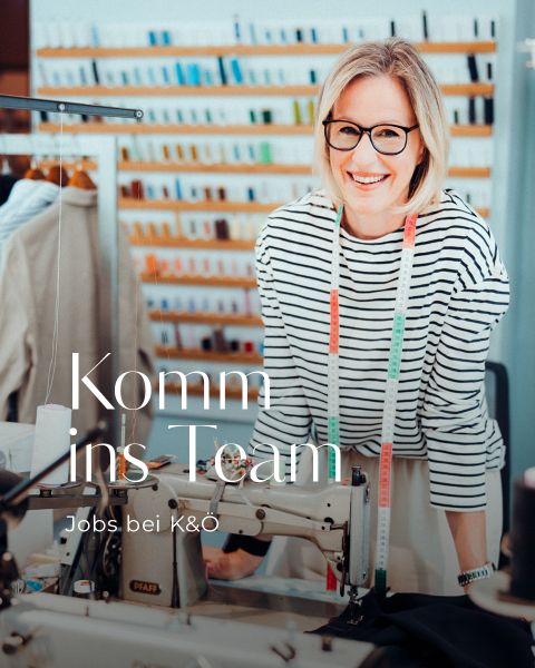Eine lächelnde Frau mit Brille und einem gestreiften Hemd steht an einer Nähmaschine mit bunten Fäden im Hintergrund. Der deutsche Text auf dem Bild lautet: "Komm ins Team. Jobs bei K&Ö.