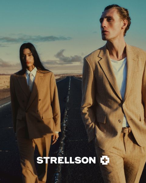 Ein Mann und eine Frau in eleganten braunen Anzügen gehen bei Sonnenuntergang über eine leere Straße. Das Strellson-Logo erscheint am unteren Rand des Bildes.