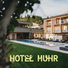 Ein modernes Hotel mit Holzbalkonen blickt auf einen rechteckigen Außenpool, der von Liegestühlen und grünem Rasen umgeben ist. Im Hintergrund sind Bäume und Hügel zu sehen. Der Text lautet "HOTEL MUHR.