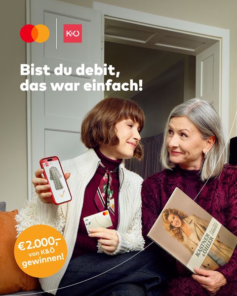 Eine jüngere Frau zeigt einer älteren Frau ihr Telefon, auf dem ein Häkchen und eine Debitkarte angezeigt werden. Die ältere Frau lächelt und hält eine Zeitschrift in der Hand. Der Text lautet: "Bist du debit, das war einfach! 2.000 € von K&Ö gewinnen!" und Mastercard/K&Ö-Logos erscheinen.
