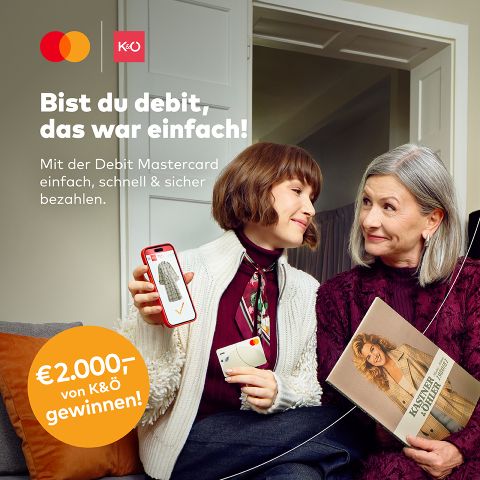 Eine junge Frau zeigt einer älteren Frau ihr Handy-Display, während sie beide lächelnd auf einer Couch sitzen. Das Bild wirbt für die Verwendung einer Debit Mastercard mit deutschem Text und einer 2.000-Euro-Promotion.