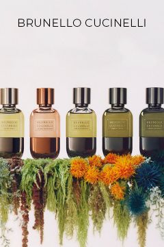 Fünf Parfümflakons von Brunello Cucinelli in verschiedenen Farbtönen stehen in einer Reihe auf einem Bett aus buntem Moos und Blumen, darüber steht auf weißem Hintergrund "Brunello Cucinelli".