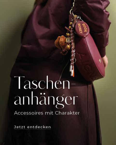 Eine Person in burgunderrotem Outfit hält eine passende Handtasche mit einer Quaste und verschiedenen schrulligen Taschenanhängern. Der deutsche Text lautet: "Taschenanhänger-Accessoires mit Charakter. Jetzt entdecken.".