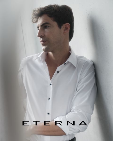 Ein Mann in einem weißen Hemd lehnt an einer hellen Wand und schaut nachdenklich zur Seite. Am unteren Rand des Bildes steht das Wort "ETERNA".