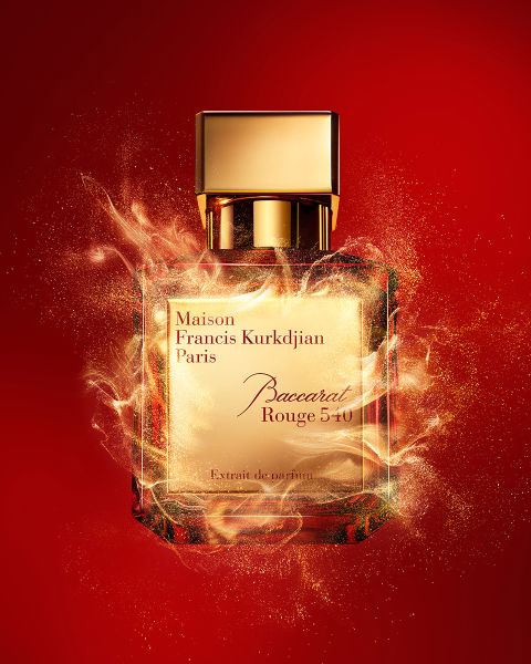 Ein Flakon des Parfums Maison Francis Kurkdjian Paris Baccarat Rouge 540 steht vor einem leuchtend roten Hintergrund, umgeben von dynamischen, goldenen Glitzereffekten, die das luxuriöse Gefühl des Duftes unterstreichen.