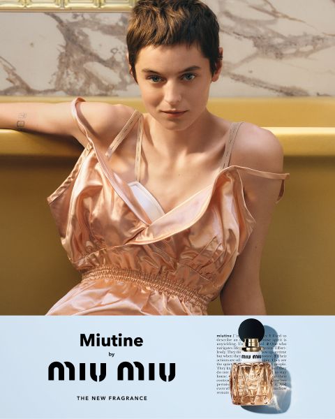 Eine Person mit kurzen Haaren und einem ärmellosen, seidigen rosa Kleid sitzt auf einer gelben Couch. Darunter sind ein Miu Miu-Parfümflakon und der Text "Miutine by MIU MIU THE NEW FRAGRANCE" zu sehen.