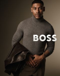 Ein Mann in einem grauen Rollkragenpullover hält eine braune Lederjacke über den Arm und schaut selbstbewusst in die Kamera. Das Wort "BOSS" erscheint in fetten weißen Buchstaben neben ihm auf einem neutralen Hintergrund.