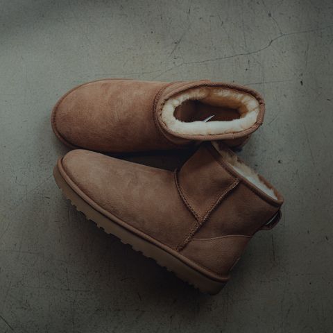 Ein Paar hellbraune Wildleder-Winterstiefel mit dickem, hellem Fleecefutter, die auf einem grauen, leicht rissigen Betonboden stehen.