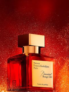Ein Flakon des Parfums Maison Francis Kurkdjian Paris Baccarat Rouge 540 mit einer goldenen Kappe steht vor einem leuchtend roten und goldenen Hintergrund.