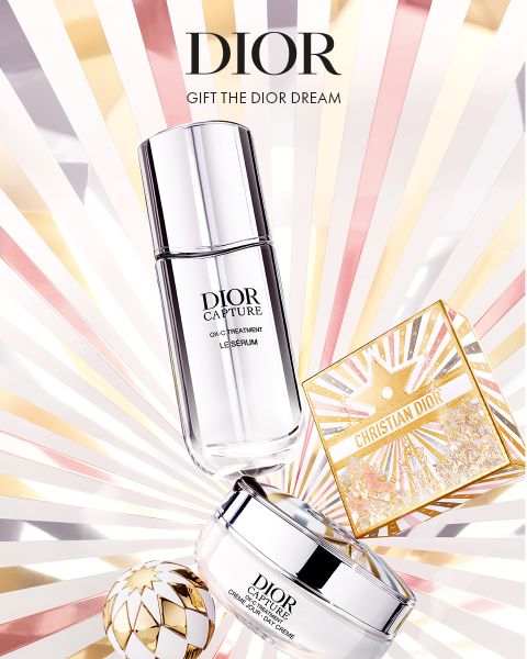Die Hautpflegeprodukte von Dior, darunter ein Serum, eine Creme und eine dekorative goldene Schachtel, werden auf einem strahlenden Hintergrund mit hellrosa, goldenen und weißen Strahlen dargestellt. Der Text lautet: "DIOR. VERSCHENKEN SIE DEN DIOR-TRAUM.