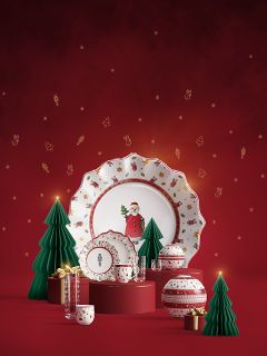 Festliches Geschirr mit Weihnachtsmann- und Weihnachtsmotiven wird mit grünen Papierbäumen, goldenen Geschenkschachteln und roten Ornamenten vor einem roten Hintergrund mit goldenen Festtagssymbolen dargestellt.