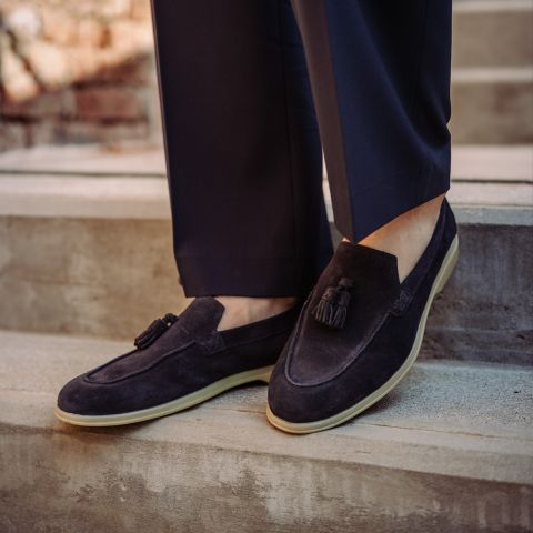 Eine Person, die schwarze Wildlederschuhe mit Quasten und eine dunkle Hose trägt, steht auf einer Betontreppe im Freien.