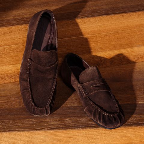 Ein Paar braune Wildlederschuhe, die auf hölzernen Stufen ausgestellt sind und deren Textur durch Licht und Schatten hervorgehoben wird.