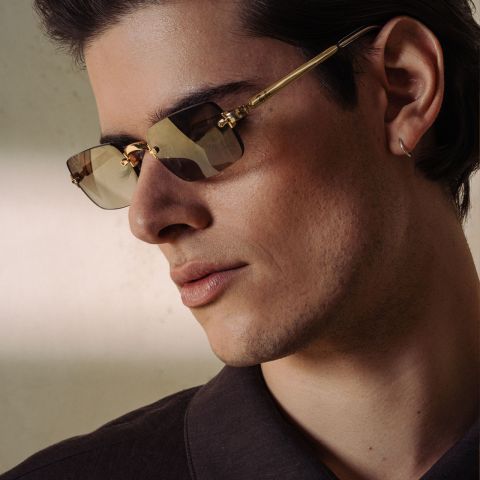 Mann mit Sonnenbrille mit goldenem Rand und dunklem Hemd.