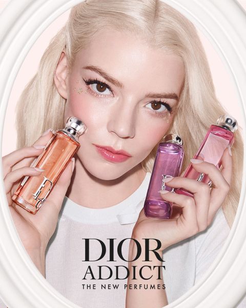 Eine Frau mit blondem Haar hält drei Dior Addict Parfümflaschen in Orange-, Rosa- und Lila-Tönen, darunter der Text "DIOR ADDICT THE NEW PERFUMES".