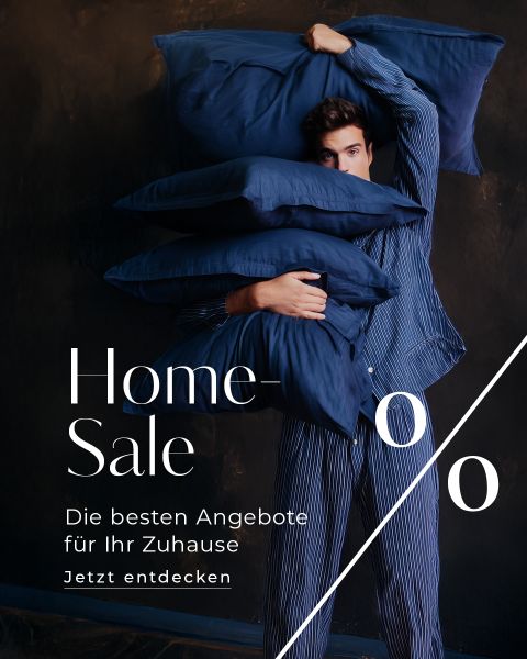 Ein Mann im gestreiften Schlafanzug hält mehrere große blaue Kissen. Der Text lautet: "Home Sale. Die besten Angebote für Ihr Zuhause. Jetzt entdecken.