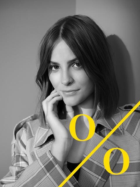 Schwarz-Weiß-Foto einer Frau mit glattem Haar, die ihr Gesicht berührt, in einer karierten Jacke, mit zwei gelben "o"-Formen und einer diagonalen Linie darüber.