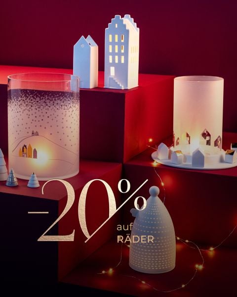 Moderne Weihnachtsdekoration mit Kerzenhaltern in Form von Häusern auf roten Podesten, umgeben von Lichterketten und einem Text-Overlay "20% auf Räder".