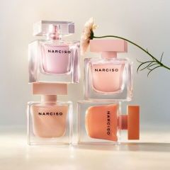 Vier Parfümflakons der Marke Narciso in Pastelltönen sind übereinander gestapelt, und eine einzelne weiße Blume neigt sich von rechts herüber.