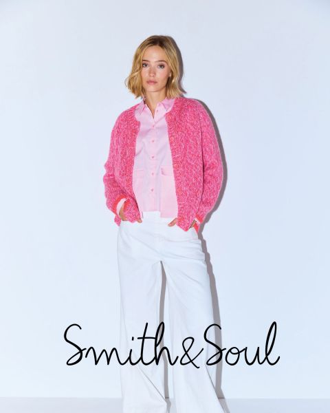 Eine Frau in einem rosa Hemd und einer Strickjacke mit weißer Hose posiert vor einem weißen Hintergrund. Der Text lautet "Smith & Soul" am unteren Rand.