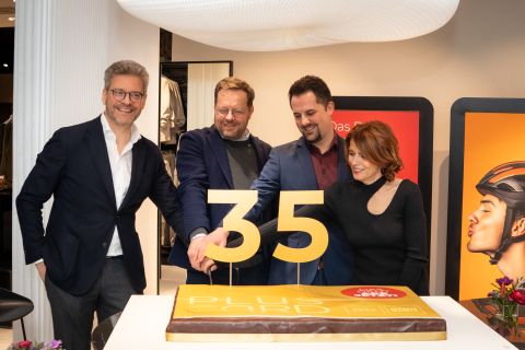 Vier lächelnde Menschen schneiden eine Torte mit einer großen goldenen "35" an und feiern einen Jahrestag in einer festlichen Umgebung.