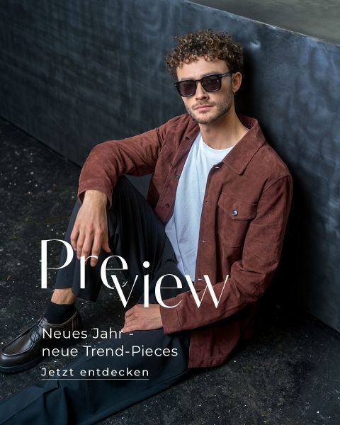Ein Mann mit Sonnenbrille, weißem Hemd und brauner Jacke sitzt auf dem Boden neben einem Tisch. Ein Text auf Deutsch wirbt für neue Trendteile für das neue Jahr.
