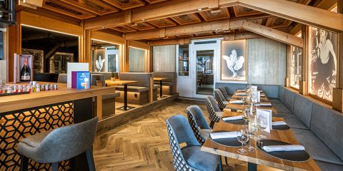 Modernes Restaurantinterieur mit Holzakzenten, eleganten Tischen mit Gläsern und Servietten, gepolsterten Stühlen, Stehplätzen und künstlerischer Wandgestaltung.