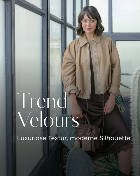 Eine Frau in einer hellbraunen Veloursjacke und einem dunklen Rock steht in einem Innenraum vor großen Fenstern und Pflanzen. Der Text lautet: "Trend Velours Luxuriöse Textur, moderne Silhouette.