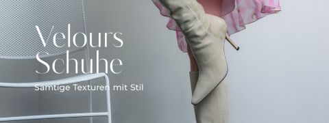 Eine Person in einem rosa durchsichtigen Kleid modelliert beigefarbene hochhackige Wildlederstiefel neben einem weißen Stuhl. Text: "Velours Schuhe, Samtige Texturen mit Stil.