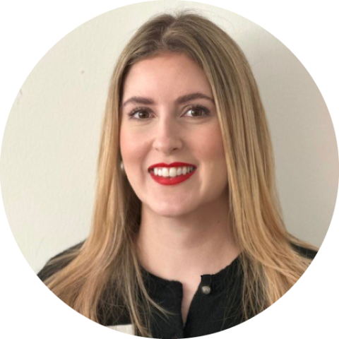 Lächelnde Frau mit langen blonden Haaren, rotem Lippenstift und einem schwarzen Oberteil vor einem schlichten weißen Hintergrund.