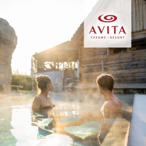 Ein Mann und eine Frau entspannen sich in einem dampfenden Außenpool in einem rustikalen Resort, mit warmem Sonnenlicht und dem Logo des Avita Therme Resorts in der Ecke.