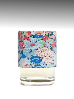 Ein gläserner Parfümflakon mit einer bunten, mit Blumen gemusterten Kappe vor einem grauen Hintergrund mit Farbverlauf.